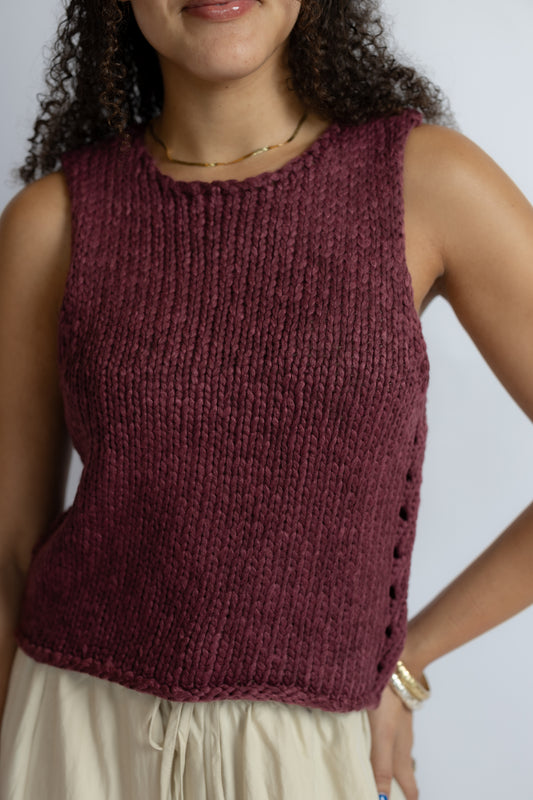 A woman wearing a sleeveless, ribbed knit top in a deep burgundy or maroon shade, paired with light beige bottoms. The photo is cropped from the chin down against a plain light gray background.
