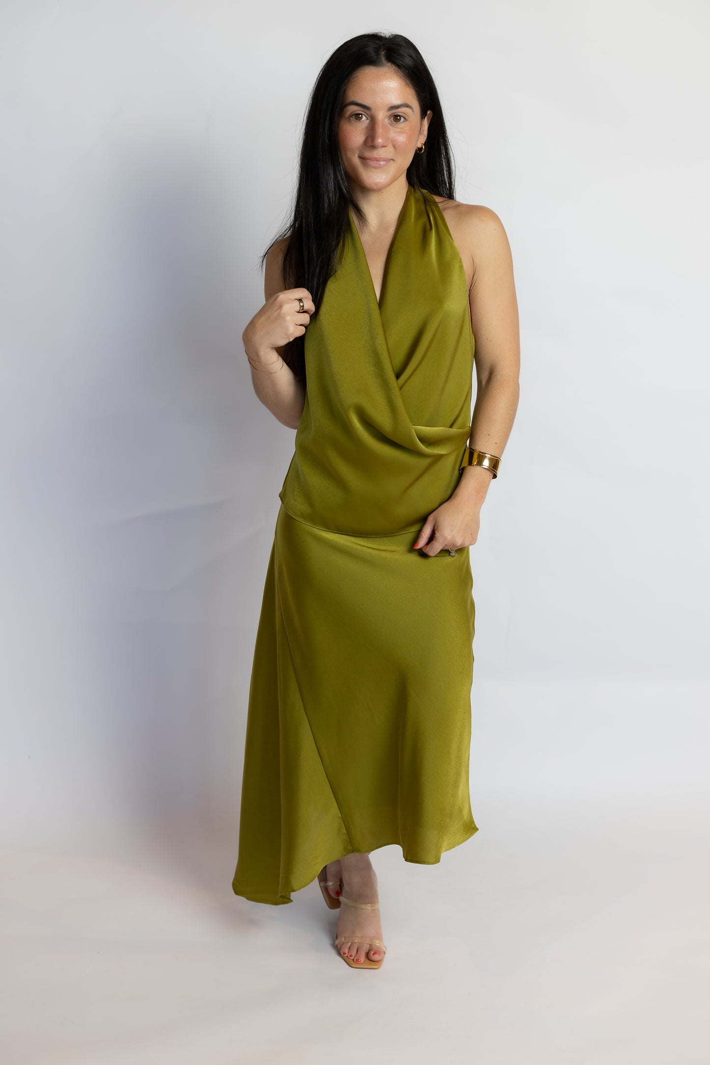 A woman modeling a sleeveless olive green halter-neck wrap maxi dress against a plain white studio background.