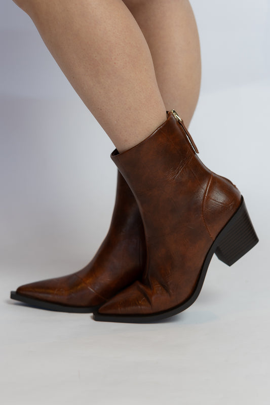 A pair of women's pointed-toe ankle boots in distressed brown leather, shown on a model's feet against a light gray studio background.