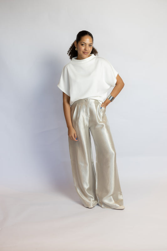 A woman modeling a white short-sleeve top and shiny light beige wide-leg satin pants against a plain light gray studio background.