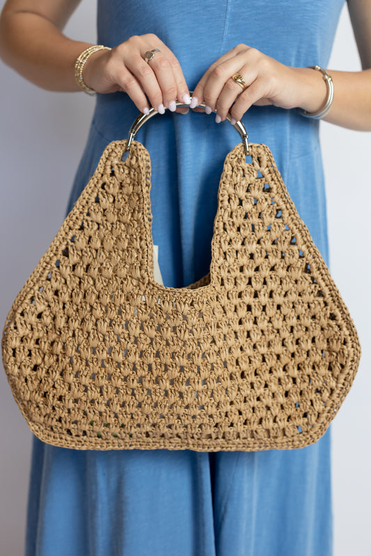 Person holding a woven handbag with a plain background