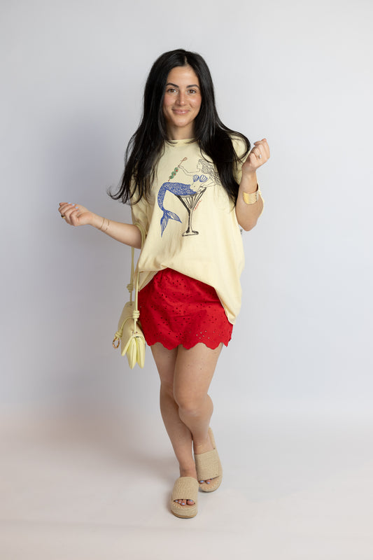 Woman wearing a yellow oversized t-shirt with a graphic design and red lace skirt on a plain background