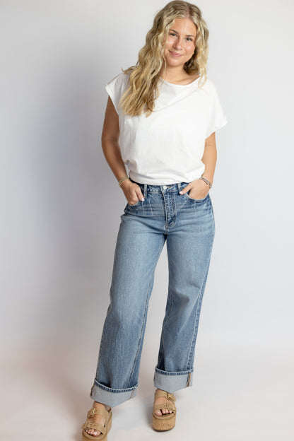 Woman wearing a white t-shirt and light blue jeans against a plain background