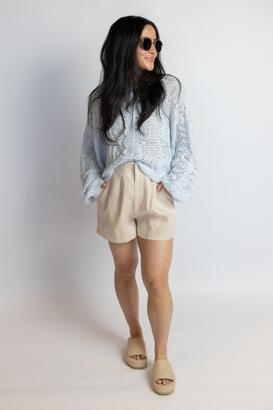Woman wearing a light blue patterned shirt, beige shorts, and sandals on a white background