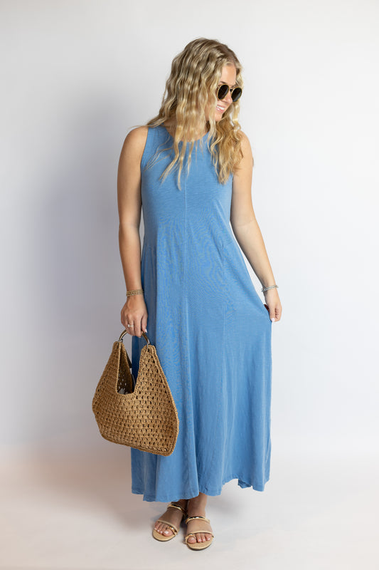 Woman wearing a blue sleeveless cotton midi dress with a relaxed silhouette and woven tote bag.
