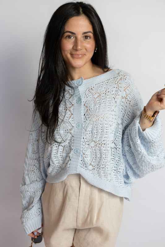 Woman wearing a light blue crochet knit cardigan with a relaxed fit and neutral linen shorts.