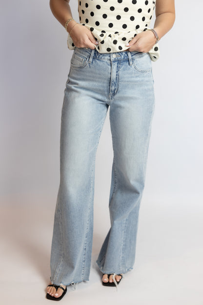 Person wearing light blue jeans and a polka dot top on a plain background