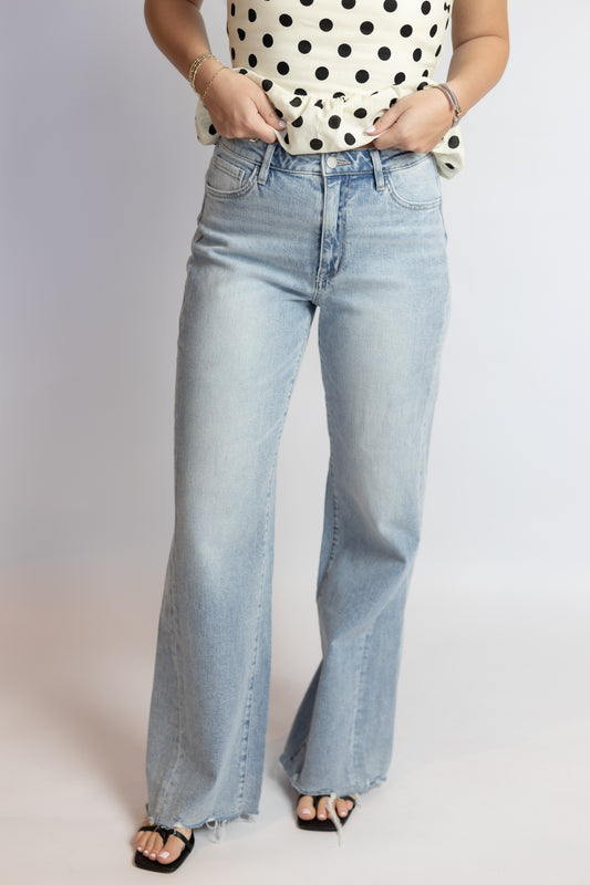 Person wearing light blue jeans and a polka dot top on a plain background