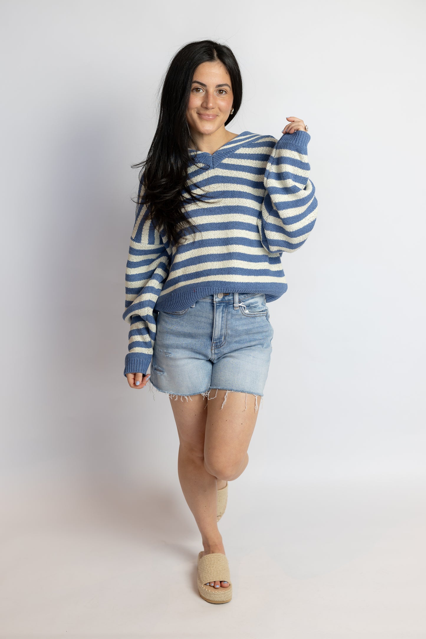 Woman wearing a blue and white striped sweater and denim shorts on a white background