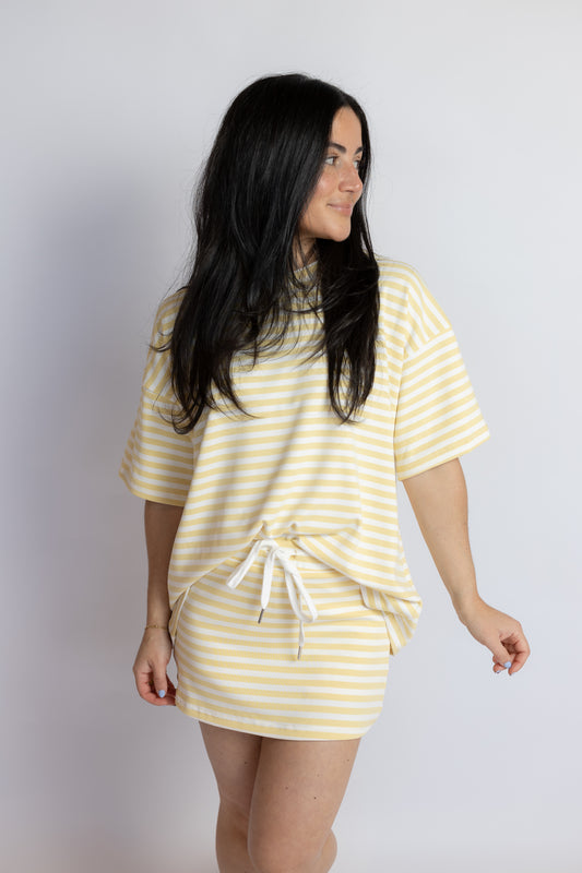 Woman wearing a yellow and white striped drawstring skort with a matching oversized striped tee and woven slide sandals.