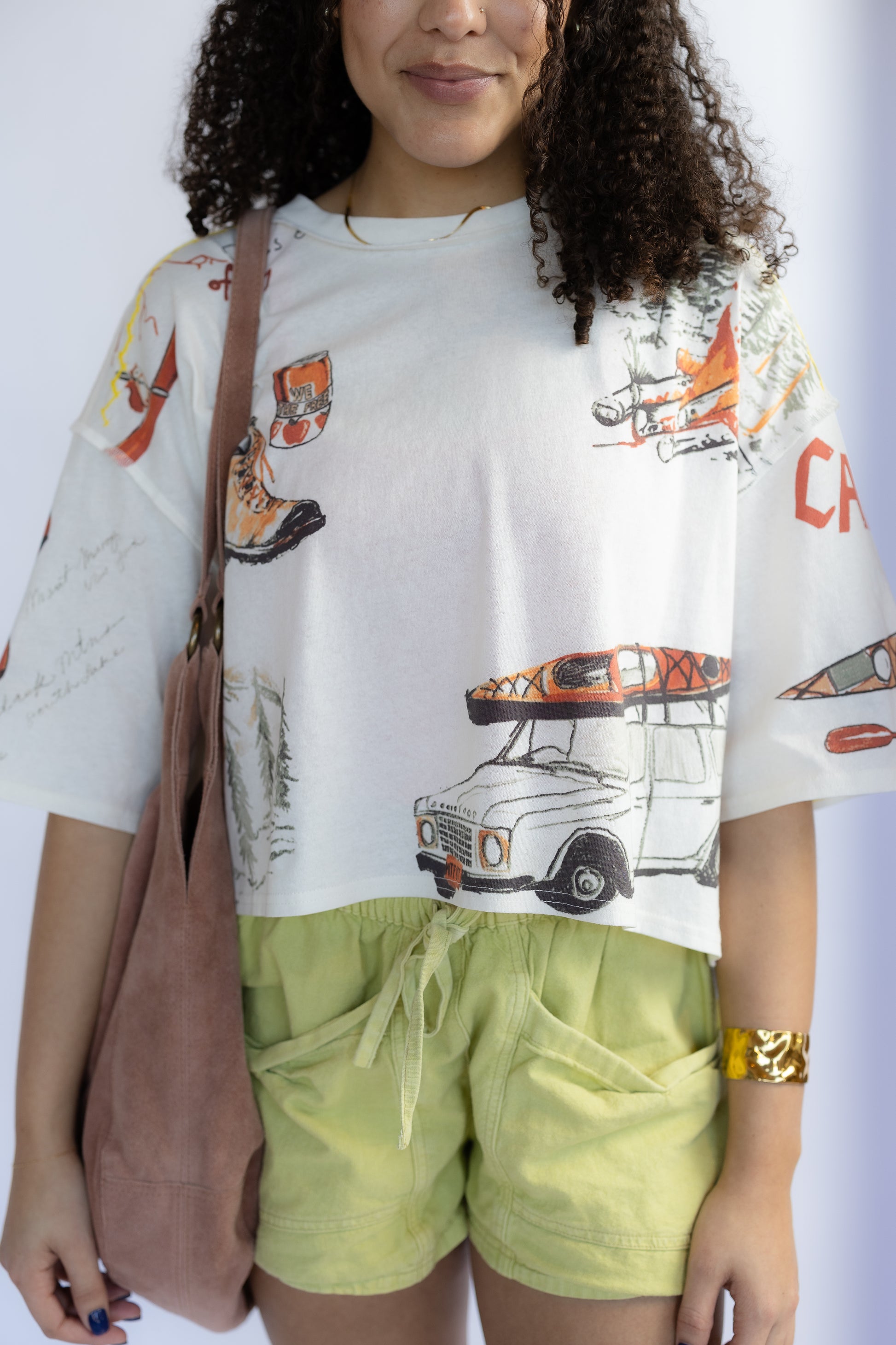 Person wearing a white t-shirt with graphic designs and light green shorts, holding a brown bag.