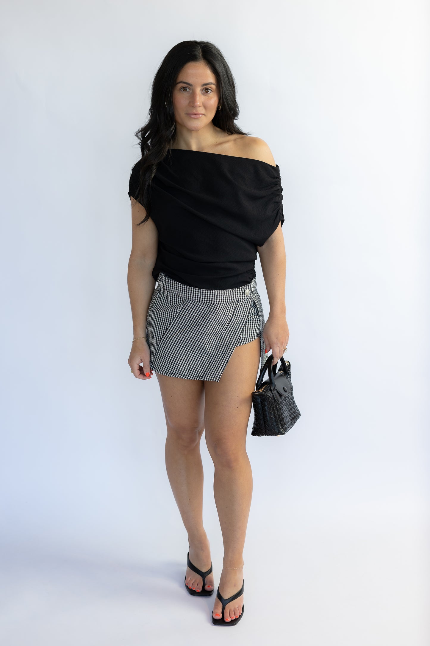 Woman wearing a black off-shoulder top and patterned skirt on a white background