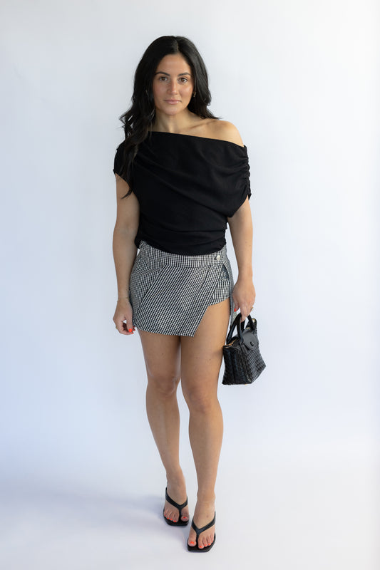 Woman wearing a black off-shoulder top and patterned skirt on a white background