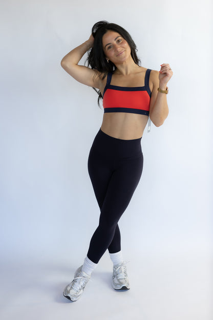 Woman wearing a red sports bra and black leggings on a white background