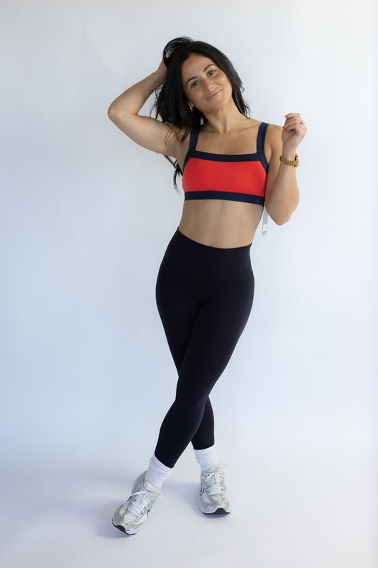 Woman wearing a red sports bra and black leggings on a white background