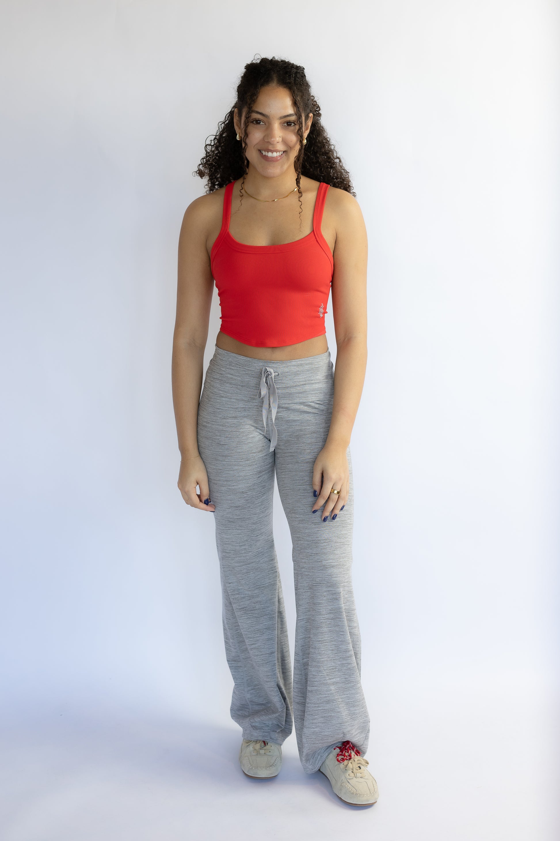 Woman wearing a red tank top and gray sweatpants on a white background