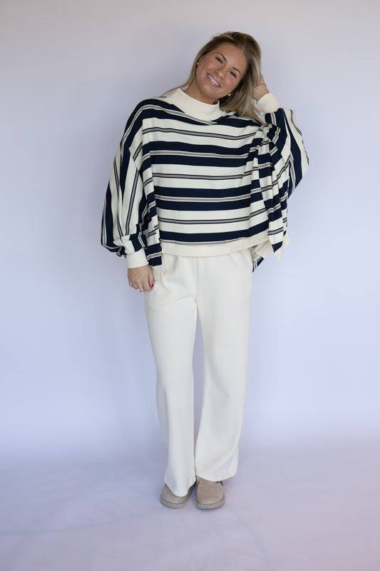 Person wearing a striped sweater and white pants against a plain background