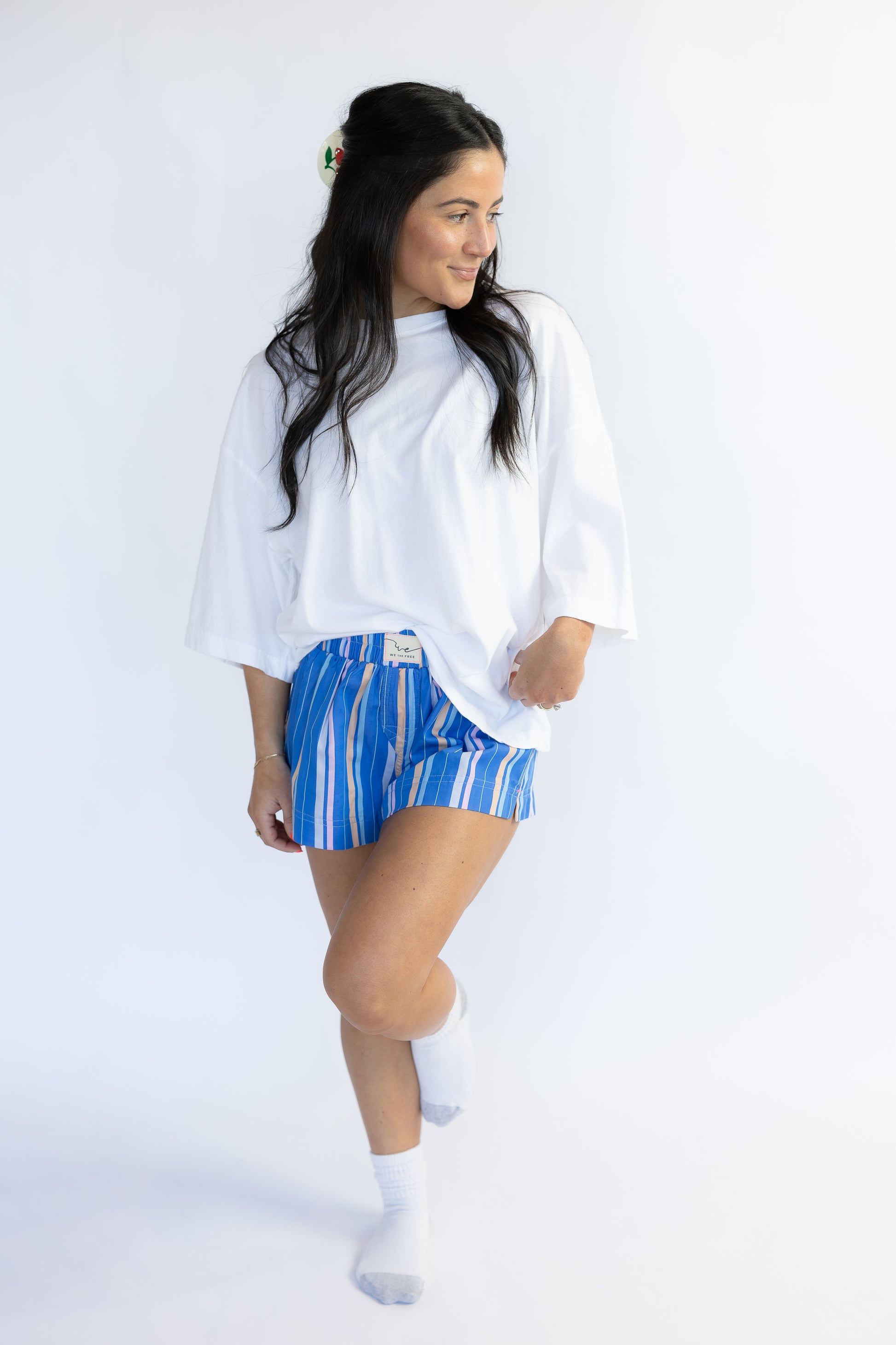 Woman wearing a white oversized shirt and blue striped shorts on a white background