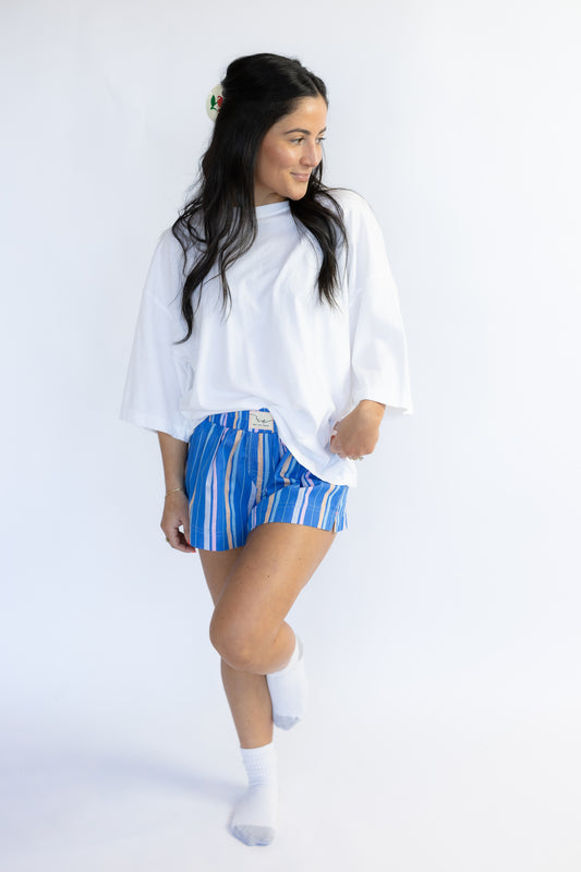 Woman wearing a white oversized shirt and blue striped shorts on a white background