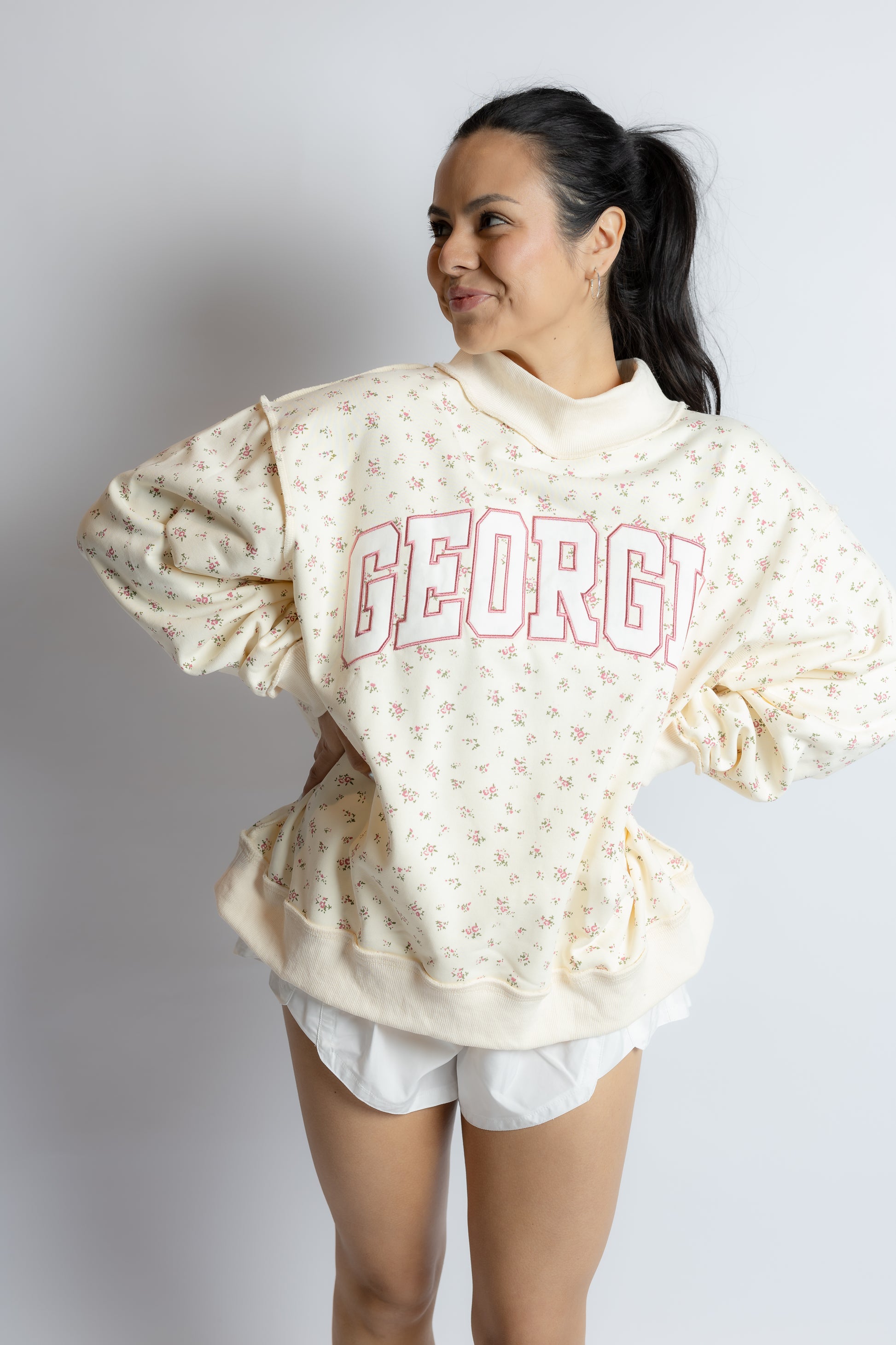 Woman wearing a cream-colored sweatshirt with 'GEORGIA' printed on it against a plain background