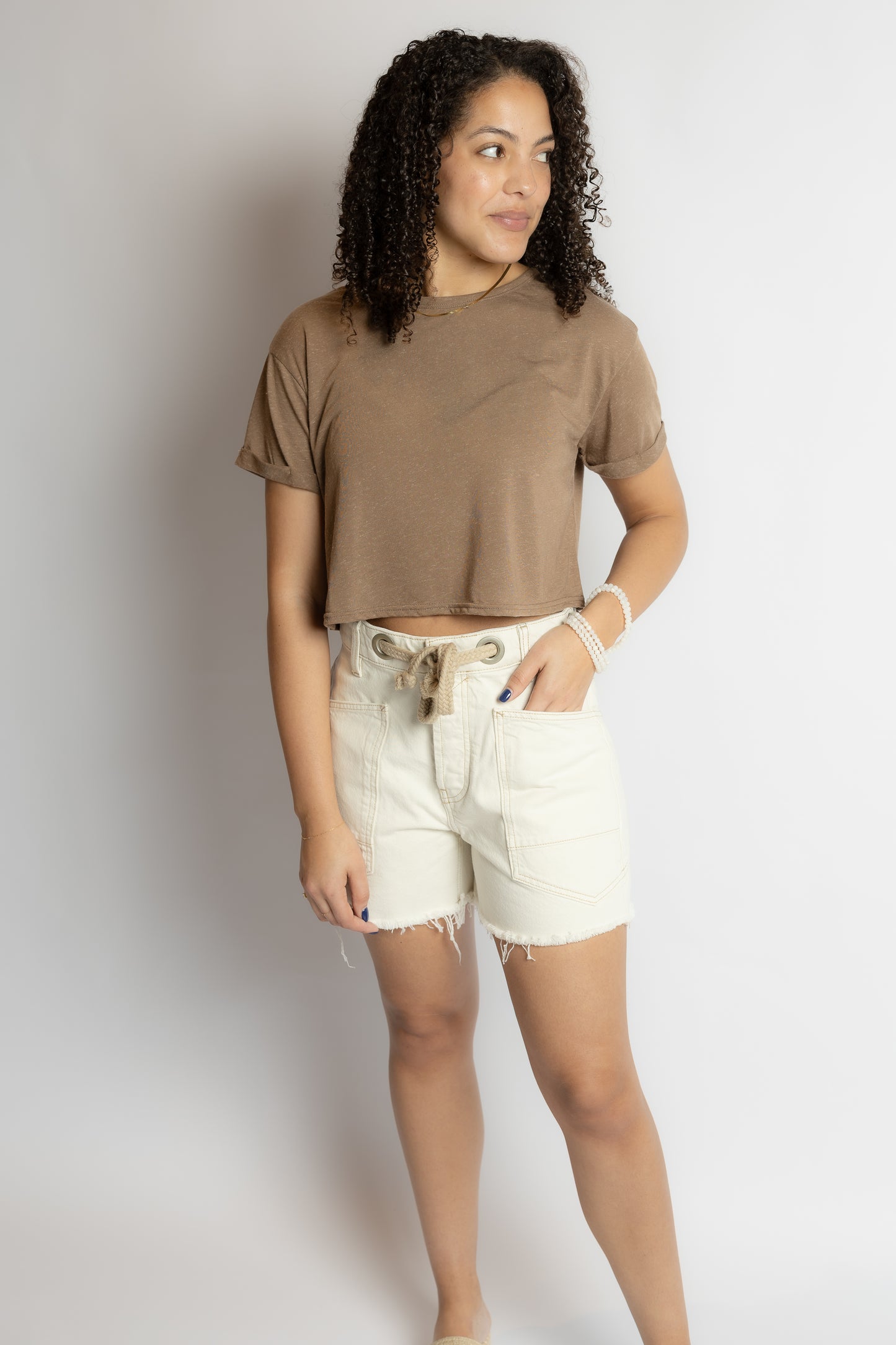 Woman wearing a brown t-shirt and white shorts against a plain background