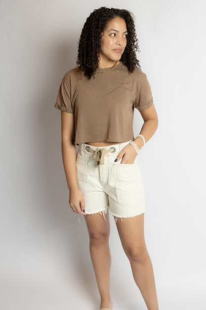 Woman wearing a brown t-shirt and white shorts against a plain background