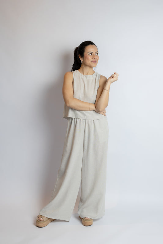 Woman wearing a beige sleeveless top and wide-leg pants against a white background