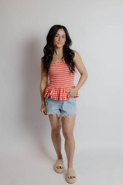Woman wearing a red checkered top and denim shorts against a plain background