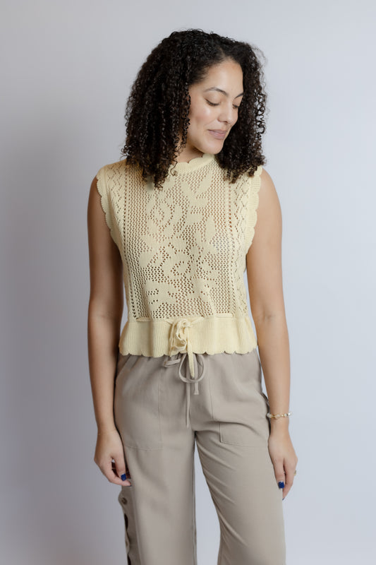 Woman wearing a light yellow sleeveless top and beige pants against a plain background