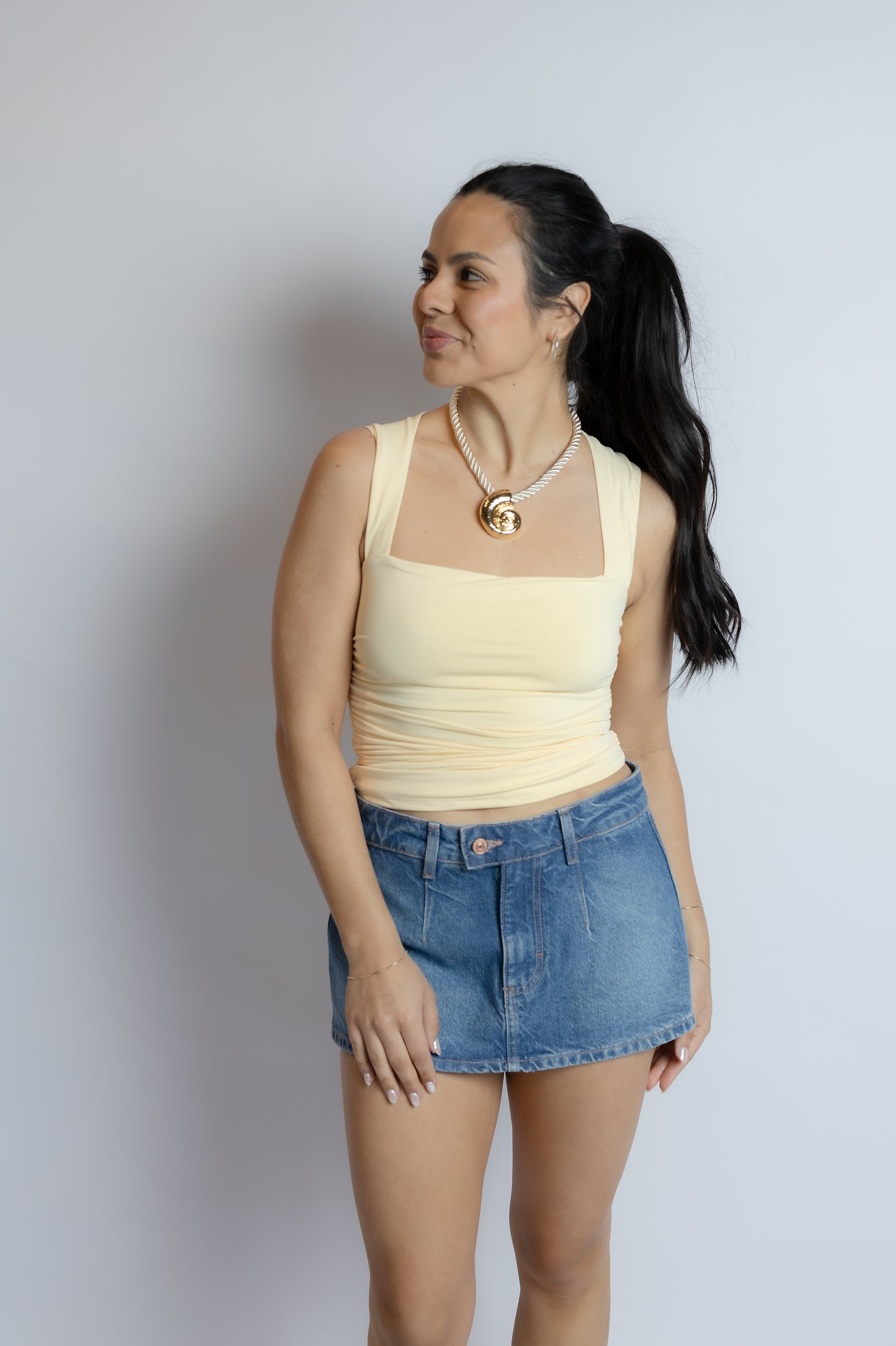Woman wearing a yellow tank top and denim skirt against a plain background