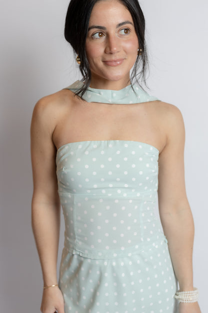 Woman wearing a light blue polka dot dress against a plain background