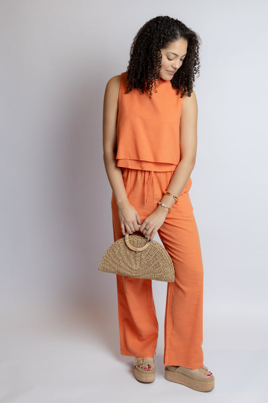 Woman in an orange outfit holding a straw bag against a white background