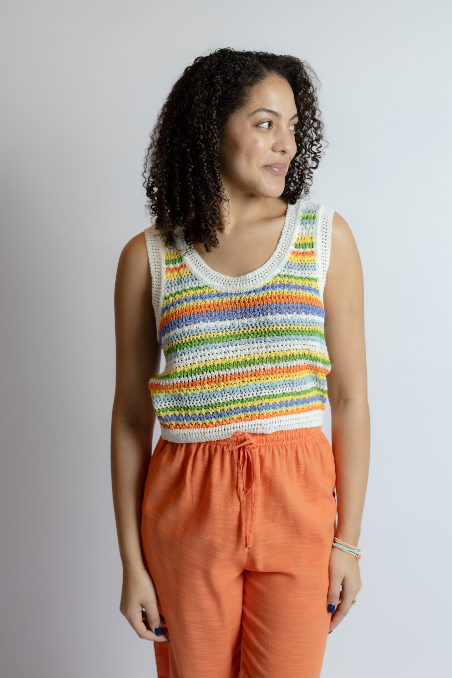 Woman wearing a colorful striped sleeveless top and orange pants against a plain background