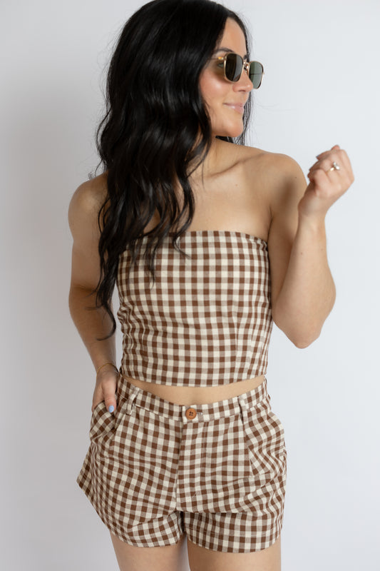 Woman wearing a brown and white checkered outfit with sunglasses on a plain background