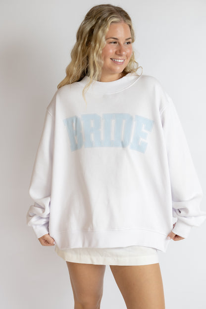 Woman wearing a white sweatshirt with blue BRIDE text on a plain background