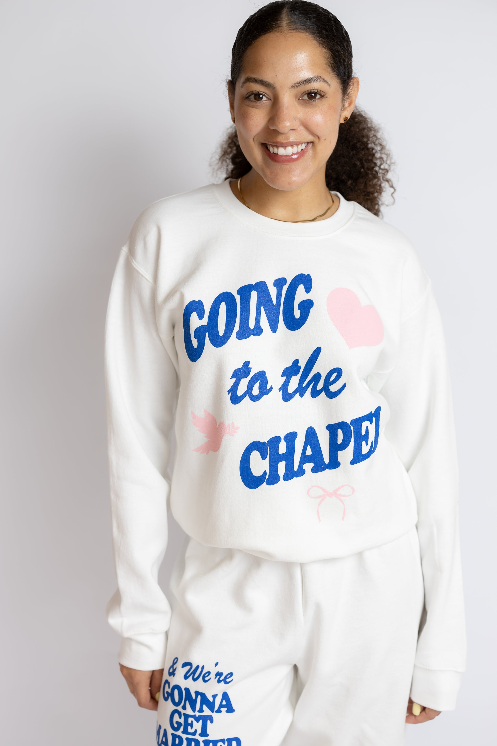 Person wearing a white sweatshirt with blue "Going to the chapel" text on a plain background