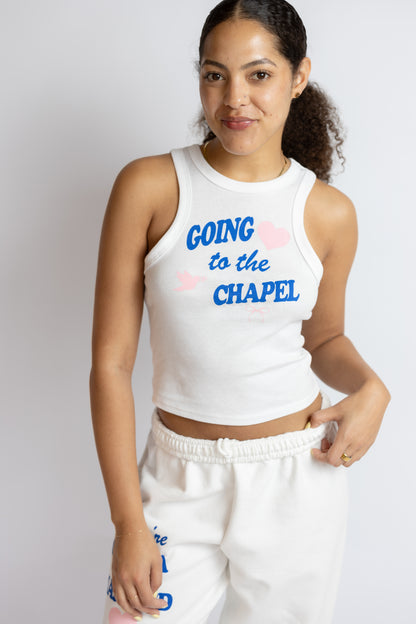 Woman wearing a white sleeveless top with "Going to the chapel" text and matching pants on a plain background