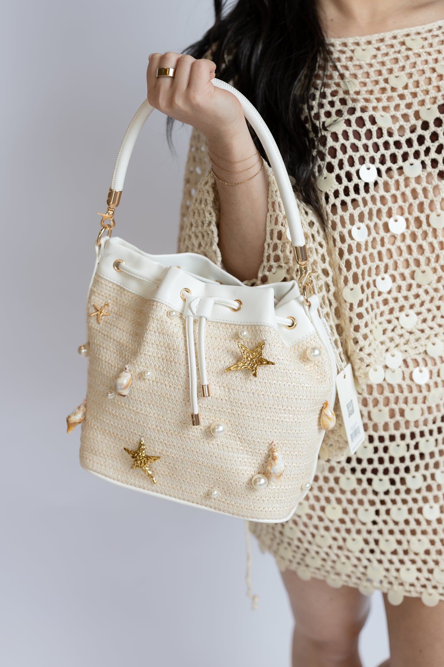 Beige handbag with shell and pearl embellishments held by a person wearing a beige crochet dress.