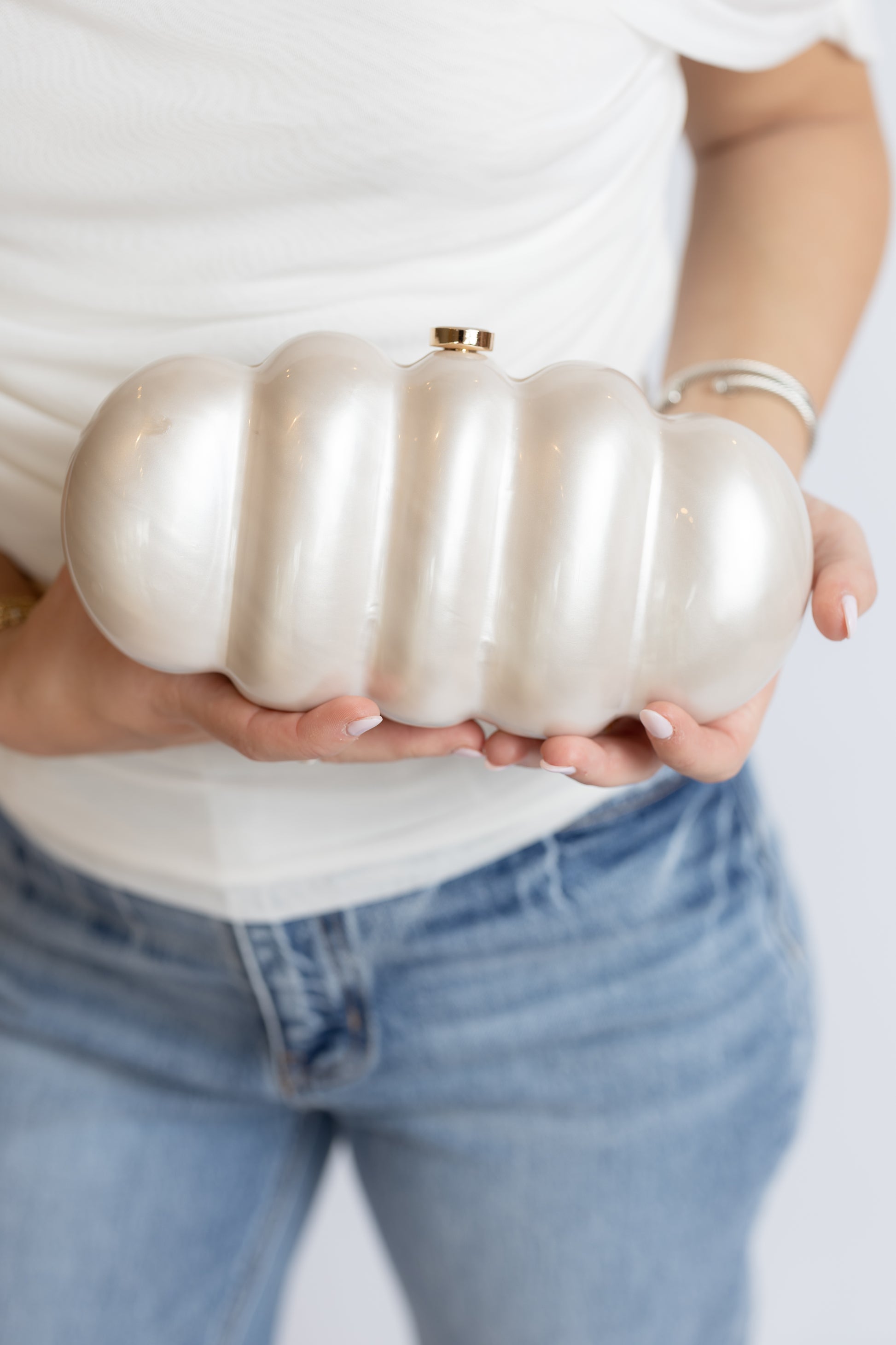 Person holding a white marble acrylic clutch against a plain background