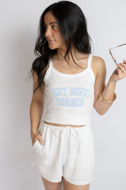 Woman wearing a white tank top with 'HOT WIFE SUMMER' text and white shorts against a plain background.