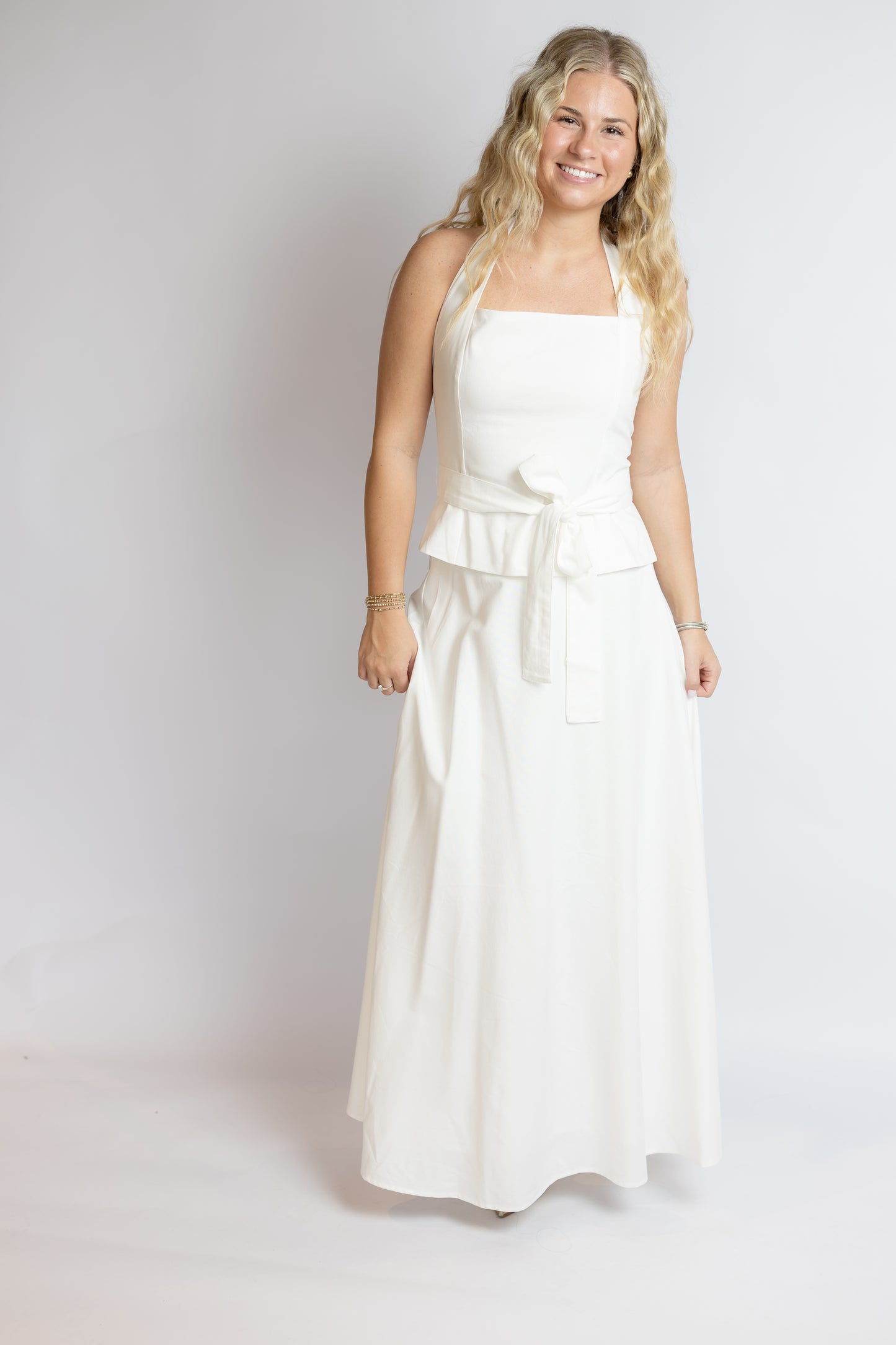 Woman wearing a white belted set against a plain background
