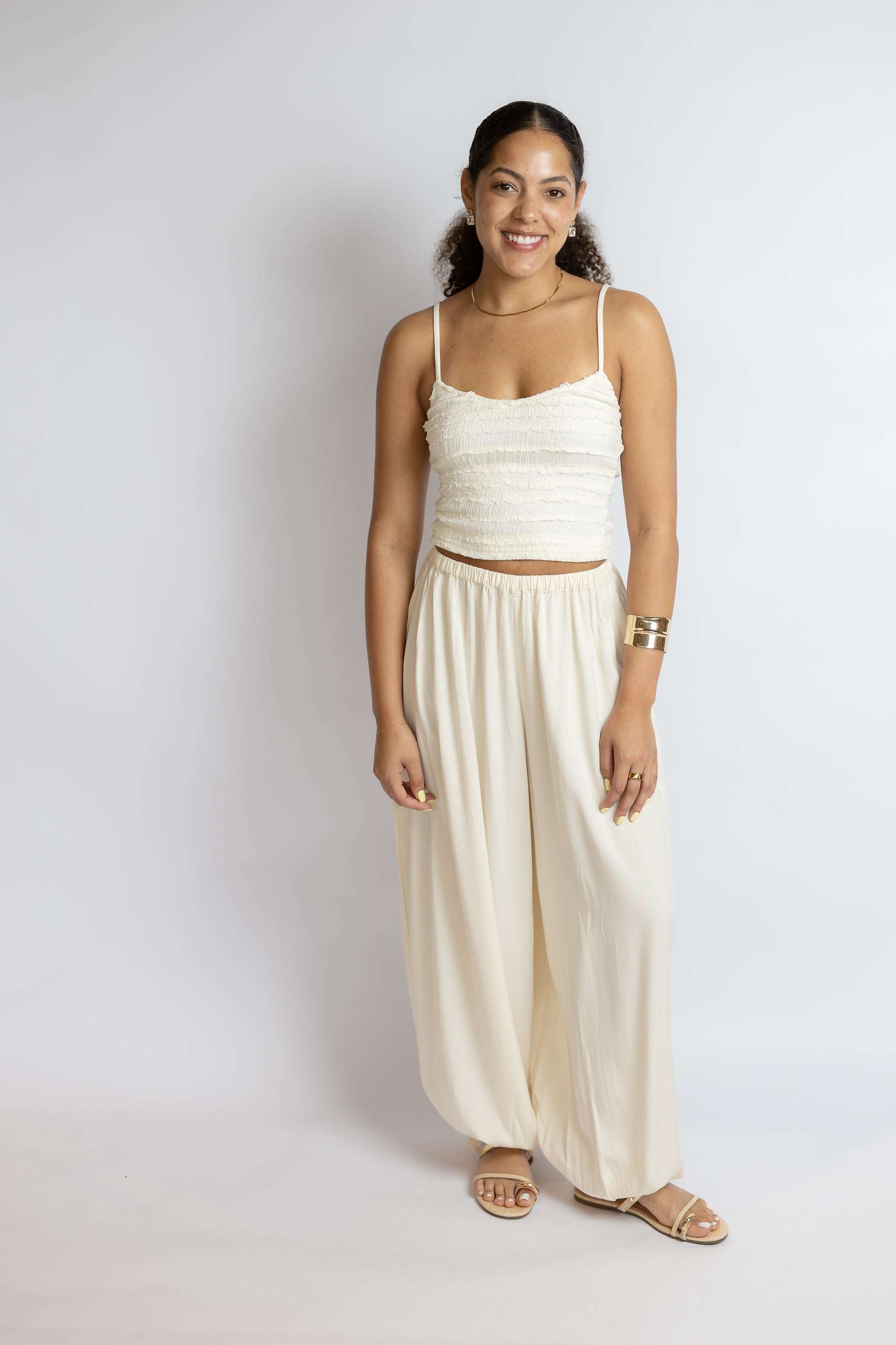Woman wearing a white top and cream pants against a plain background
