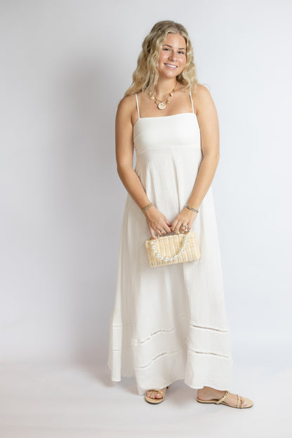 Woman in a white dress holding a beige clutch against a plain background