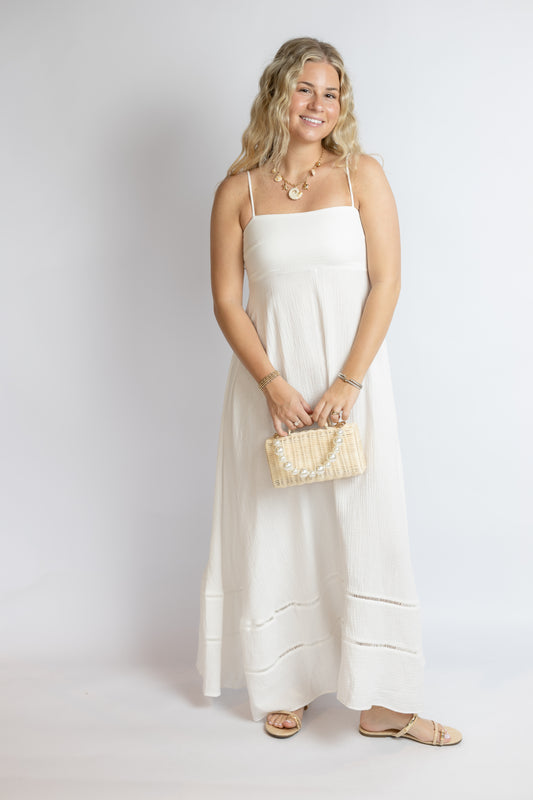 Woman in a white dress holding a beige clutch against a plain background