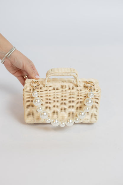 Wicker handbag with pearl embellishments held by a hand on a light background