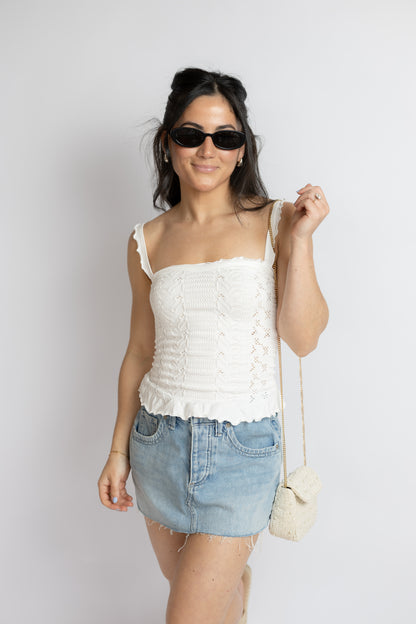 Woman wearing a white top and denim skirt with sunglasses and a small bag on a plain background