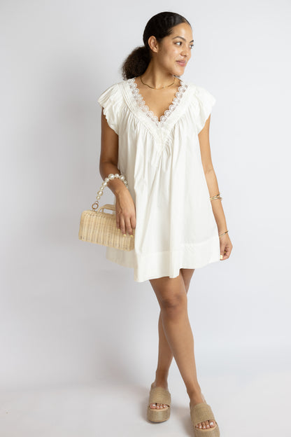 Woman wearing a white dress holding a woven handbag on a plain background