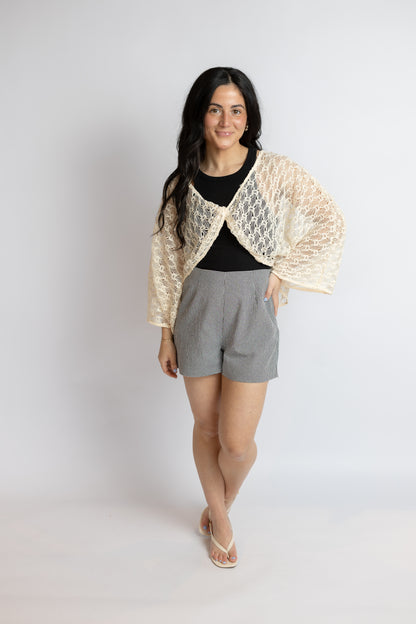 Woman wearing a beige lace shawl over a black top and gray shorts on a white background