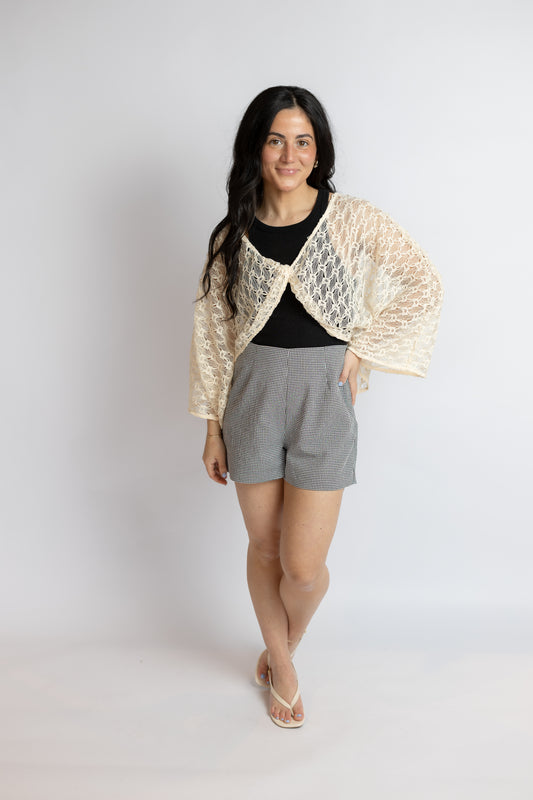 Woman wearing a beige lace shawl over a black top and gray shorts on a white background