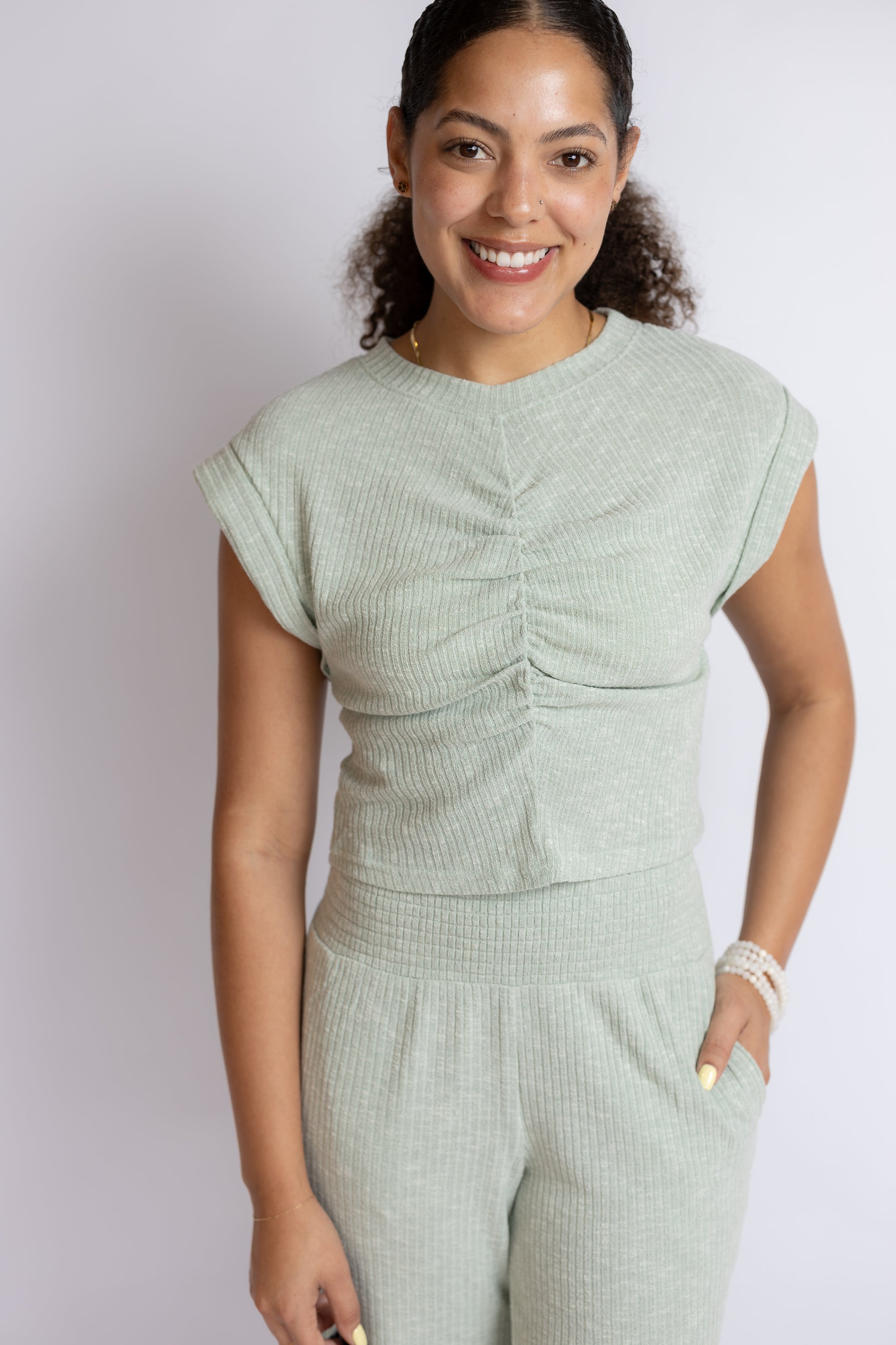 Woman wearing a light green ruched top and pants set against a plain background